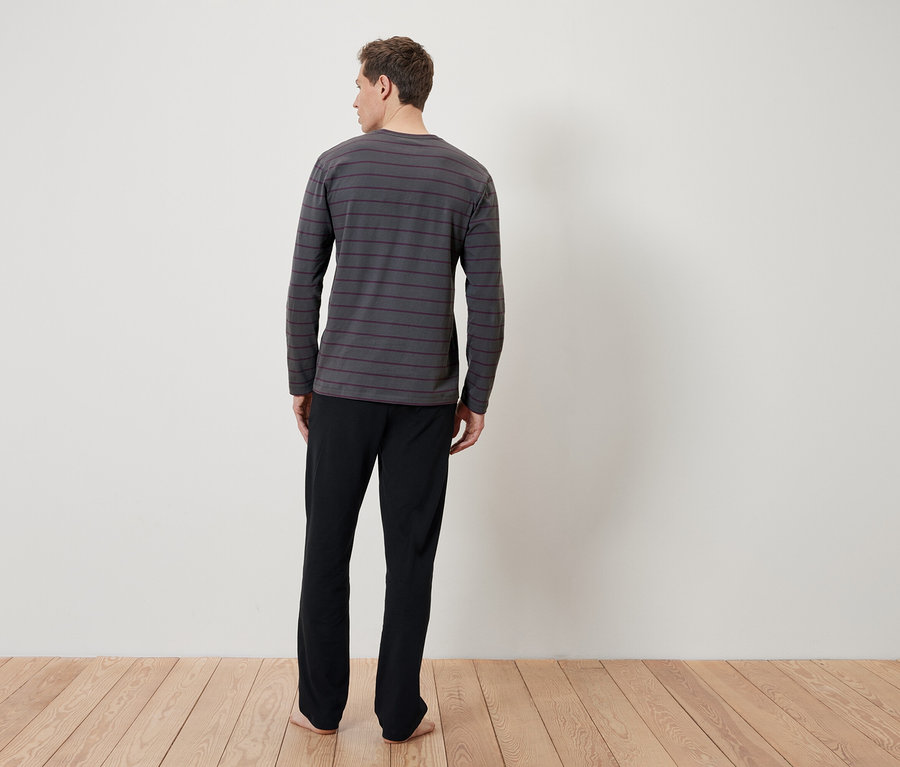 Mann von hinten trägt ein grau gestreiftes langärmeliges Schlafshirt und eine schwarze Schlafhose.