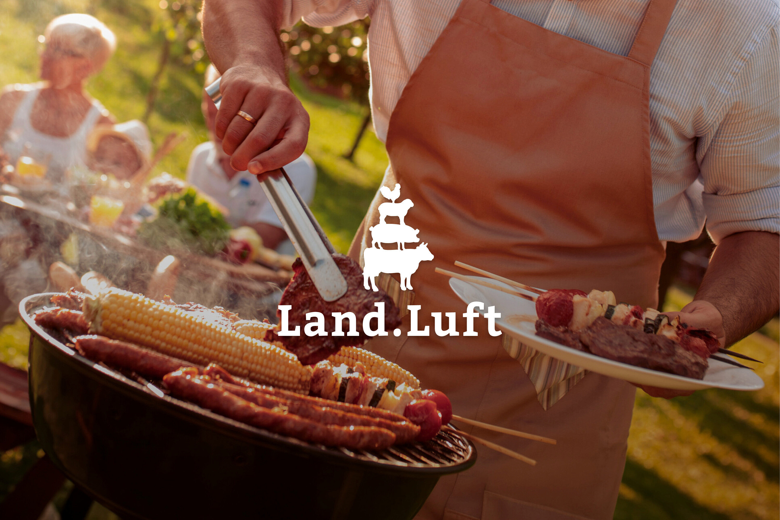 Mann grillt Steaks, Würstchen und Maiskolben im Freien, während Familie im Hintergrund sitzt. Er hält einen Teller mit Fleischspießen.