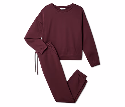 Burgunderfarbenes Set aus Sweatshirt und Jogginghose liegt auf weißem Grund.