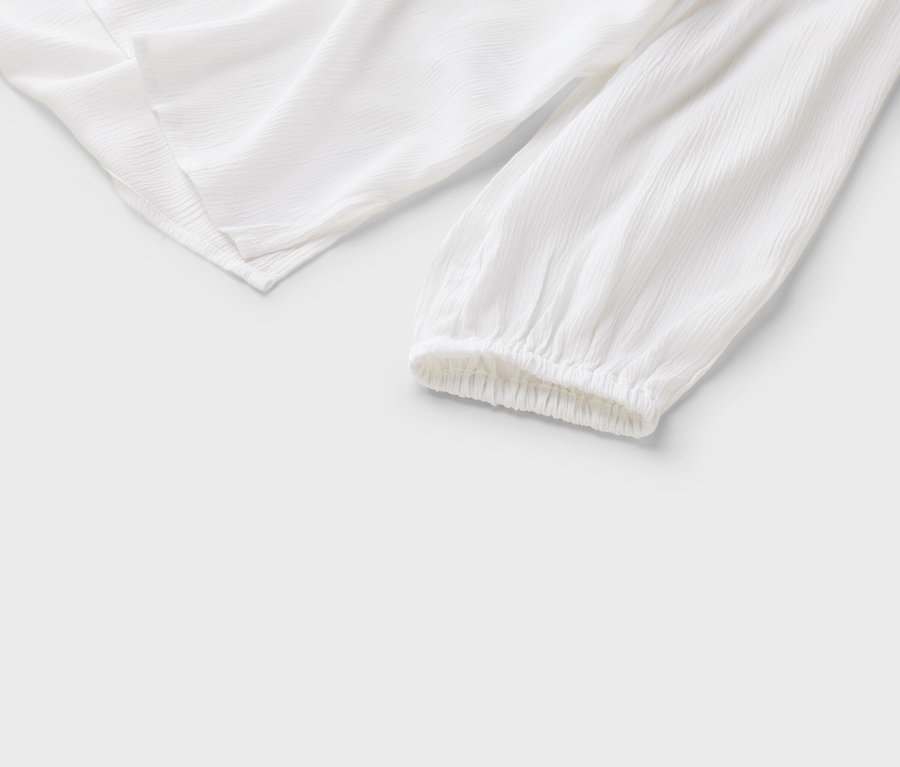 Detailansicht einer weißen Bluse mit langen Ärmeln und gerafften Bündchen auf einem weißen Hintergrund.