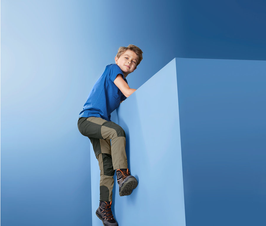 Ein Junge klettert auf einen blauen Würfel und trägt eine 2-in-1-Funktionshose.