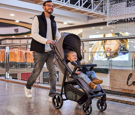 Mann schiebt einen Kinderwagen mit einem kleinen Kind darin in einem Einkaufszentrum.