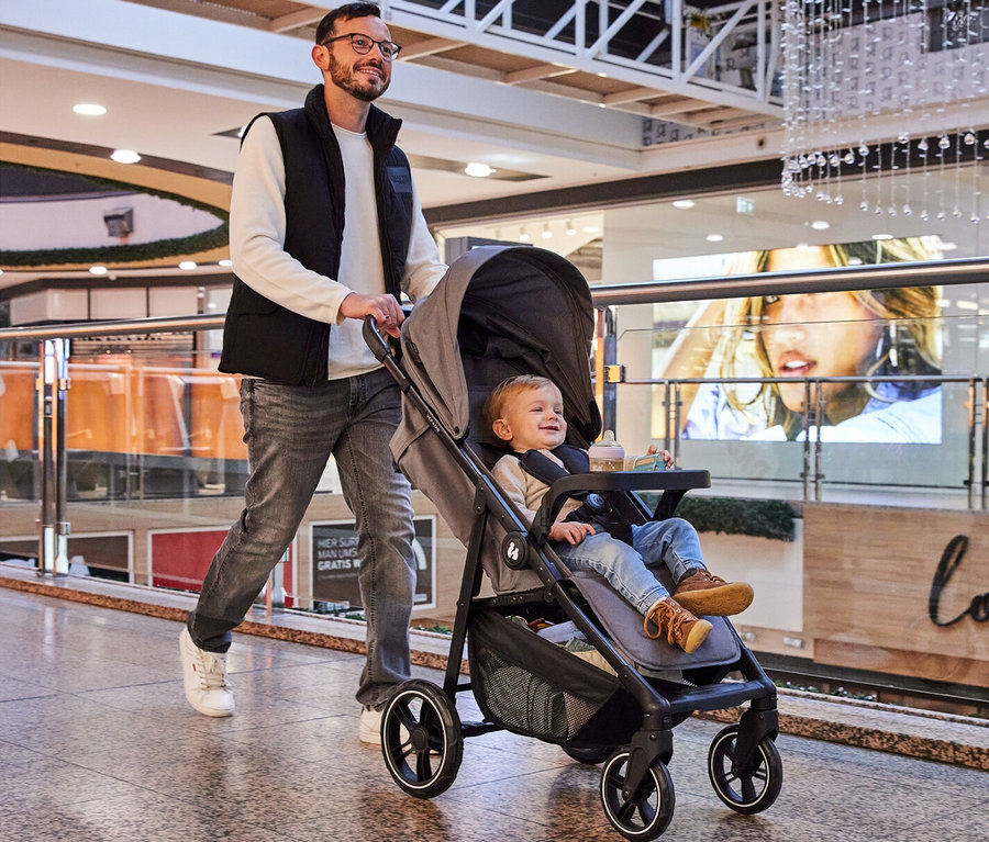 Mann schiebt einen Kinderwagen mit einem kleinen Kind darin in einem Einkaufszentrum.