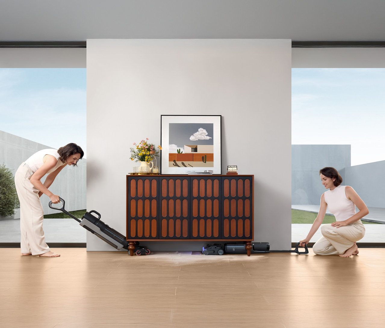 Zwei Frauen benutzen den Tineco Nass-Trockensauger »S7 Stretch Steam Plus« auf einem Holzboden vor einem Sideboard.