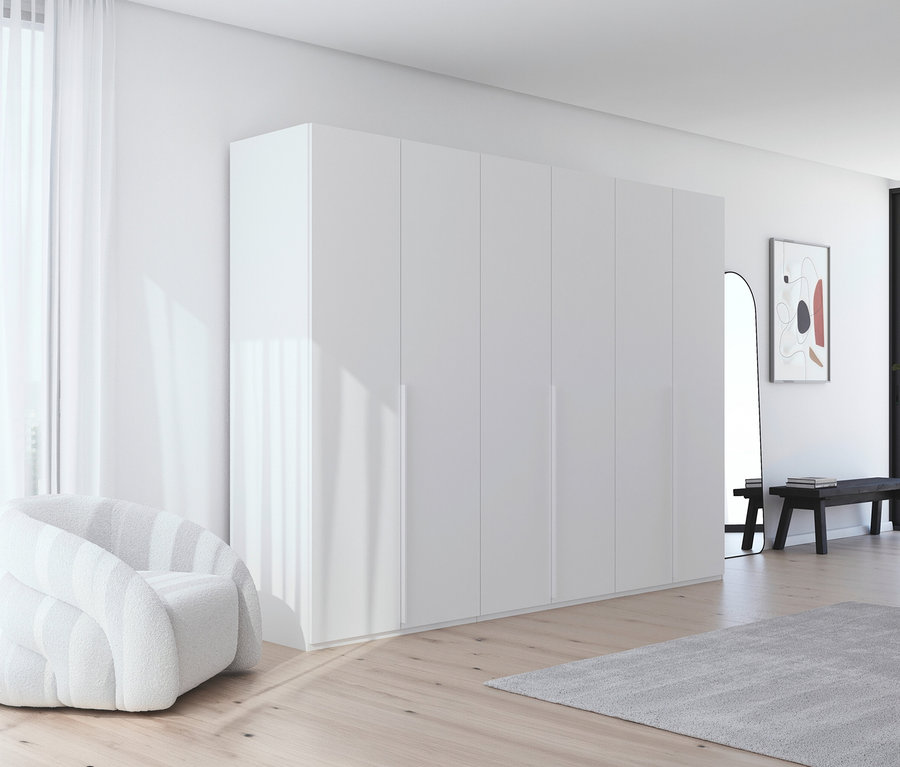 Ein helles Zimmer mit einem weißen Sessel, einem großen weißen Kleiderschrank und einem grauen Teppich auf einem Holzboden.