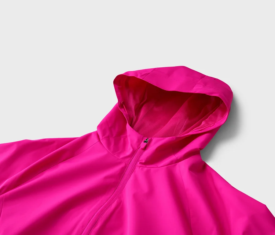 Nahaufnahme einer pinkfarbenen Jacke mit Kapuze und Reißverschluss vor einem neutralen Hintergrund.
