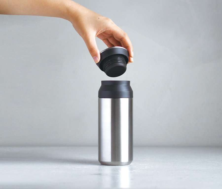 Eine Hand hält einen schwarzen Deckel über eine silberne Thermosflasche.
