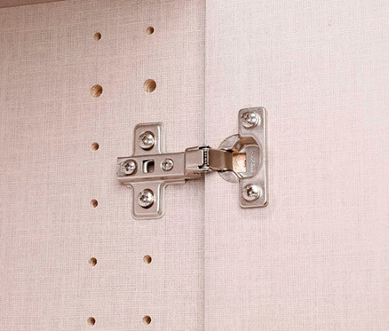 Nahaufnahme eines Möbelscharniers aus Metall an einer hellen Holzoberfläche.
