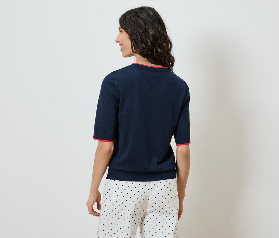 Frau von hinten, trägt marineblaues Oberteil mit roten Bündchen und gepunktete Hose.