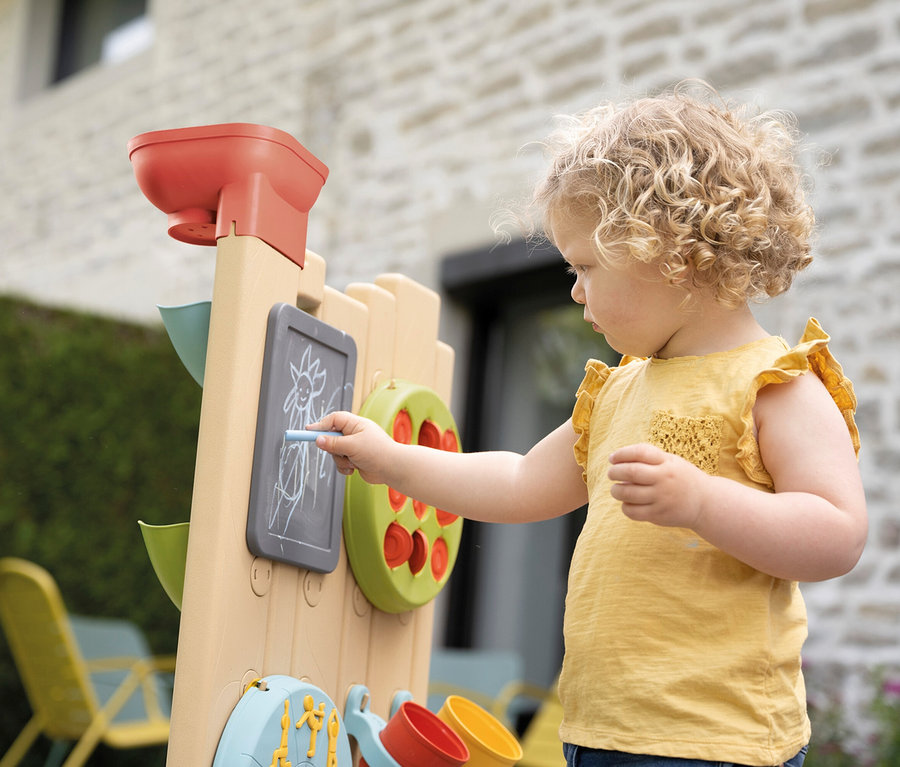Lockiges Kind zeichnet mit Kreide auf die Tafel der Smoby Life Activity Wall.