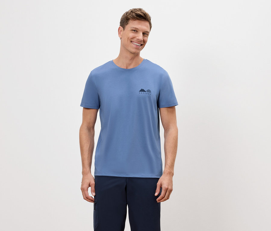 Mann trägt ein blaues T-Shirt mit einer kleinen Berg- und Regenbogen-Grafik und marineblaue Shorts.