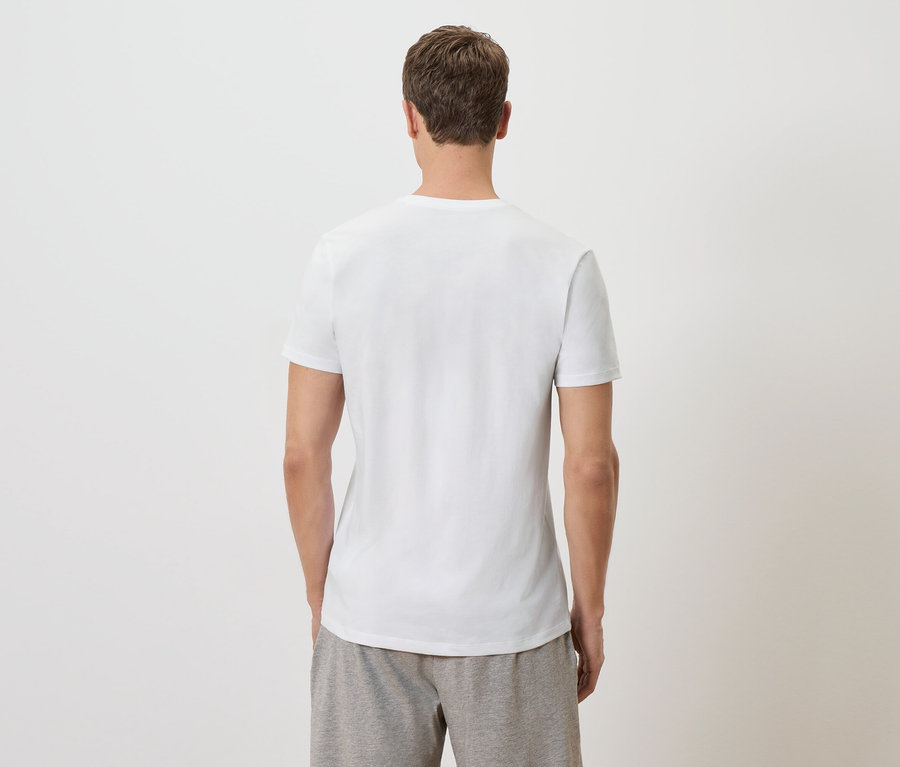 Ein Mann steht mit dem Rücken zur Kamera und trägt ein weißes T-Shirt und graue Shorts.