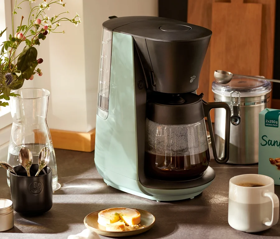 Hellgrüne »Let's Brew« Filterkaffeemaschine steht auf einer Küchentheke neben einer Tasse Kaffee und einer Blumenvase.