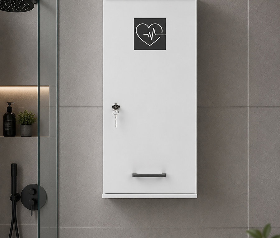 Ein weißer, wandmontierter Schrank mit Herz- und EKG-Symbol, einem Schlüssel im Schloss und einem schwarzen Griff, in einem modernen Badezimmer mit grauen Fliesen. Links sind ein schwarzer Duschkopf und Armaturen hinter einer Glaswand zu sehen, zusammen mit einem schwarzen Seifenspender und einer kleinen Pflanze auf einem Regal.