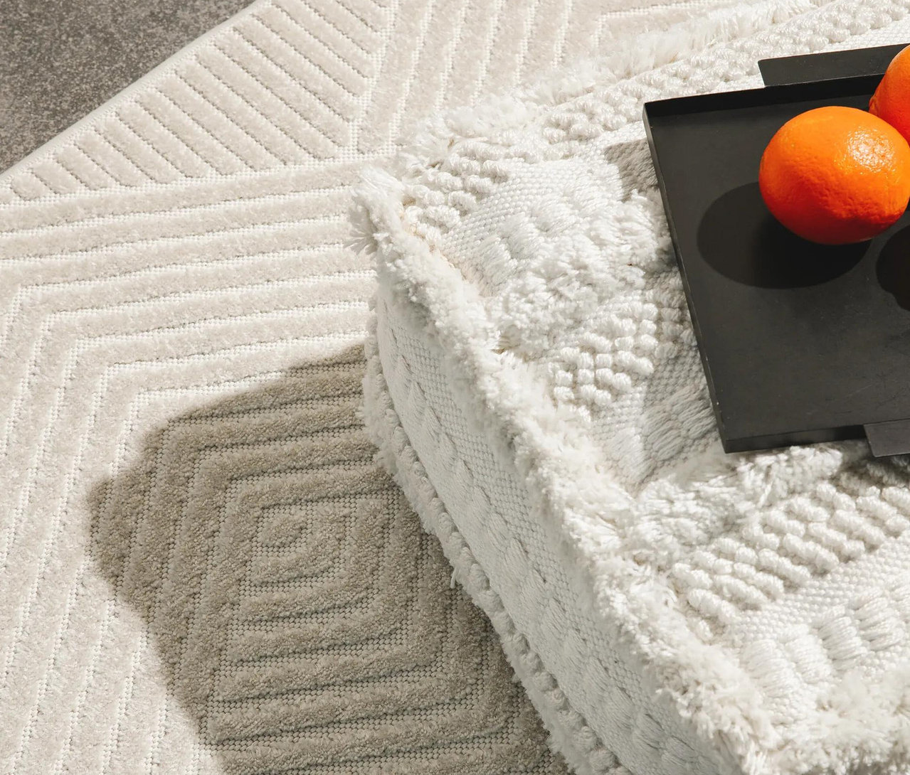 Heller benuta Indoor-Outdoor-Läufer »Mars« mit geometrischem Muster, daneben ein weißer, strukturierter Pouf mit einem schwarzen Tablett und zwei Orangen.
