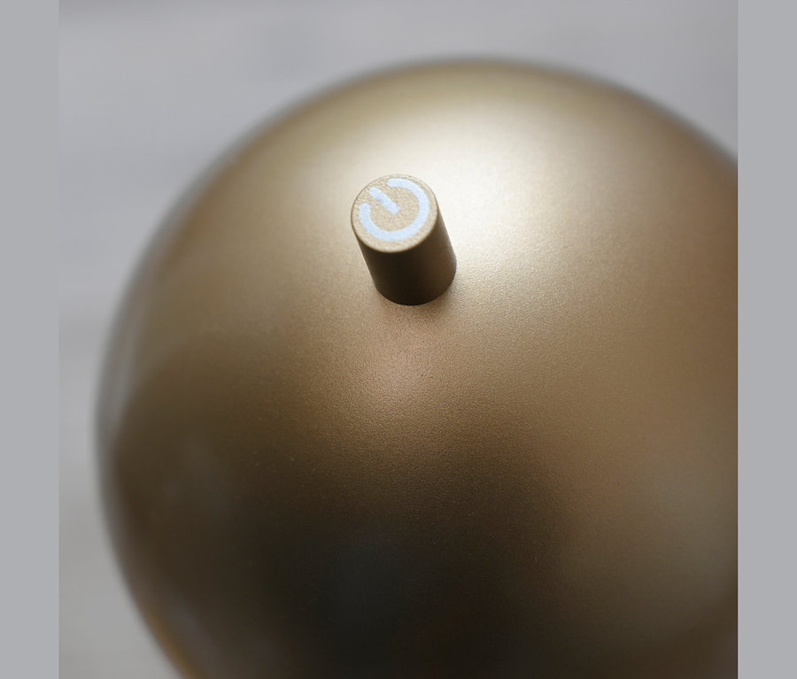 Nahaufnahme eines goldenen, kugelförmigen Objekts mit einem kleinen zylindrischen Knopf oben, der ein weißes Einschaltsymbol zeigt.