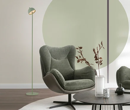 Grüner Sessel, hellgrüne SCHÖNER WOHNEN-Kollektion Akku-Stehleuchte »Bellis« und runder Couchtisch mit Deko auf weißem Teppich in einem Wohnzimmer mit hellgrünem Wandkreis.