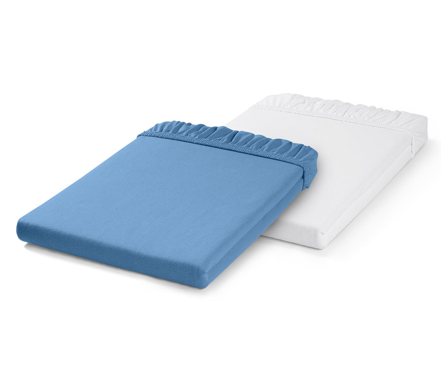 Zwei Kleinkinder-Spannbettlaken, eines blau und eines weiß, liegen übereinander.