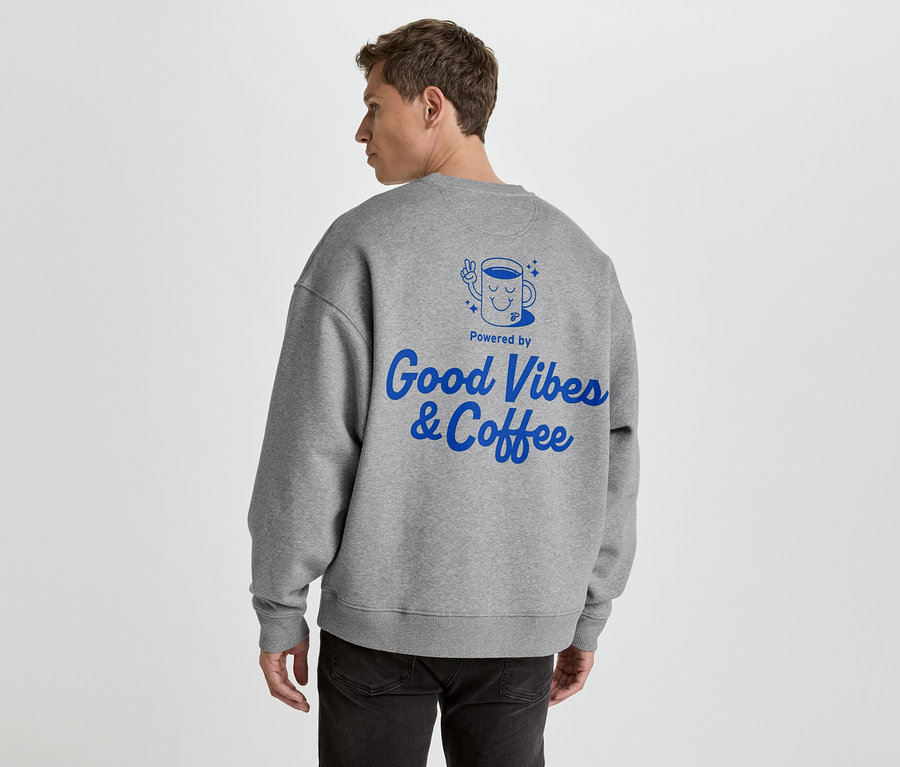 Mann von hinten in grauem Pullover mit blauem Aufdruck 'Good Vibes & Coffee'.