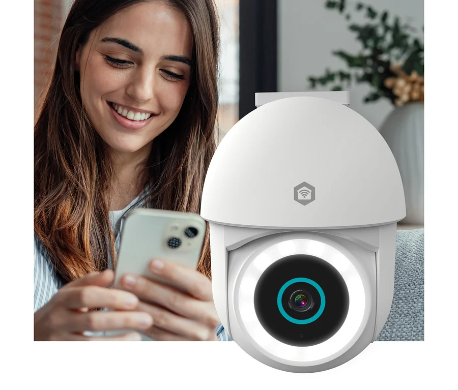 Eine lächelnde Frau blickt auf ihr Smartphone, während eine weiße Überwachungskamera mit Ringlicht im Vordergrund steht.