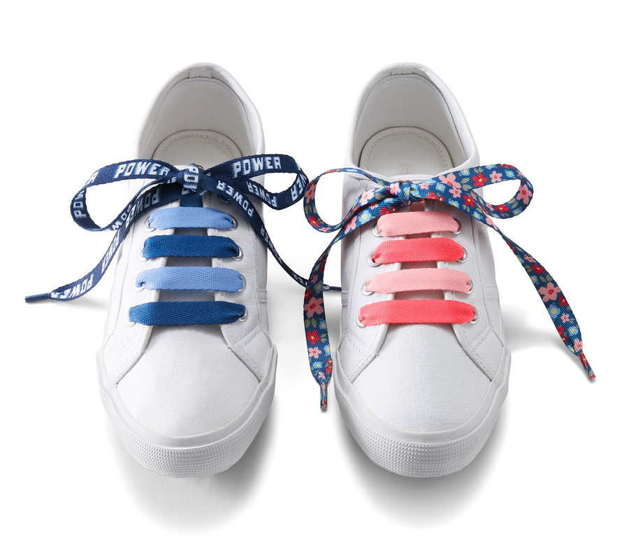 Zwei weiße Schuhe mit Kinder-Schnürsenkel mit Motiv, einmal blau und einmal mit Blumenmuster.