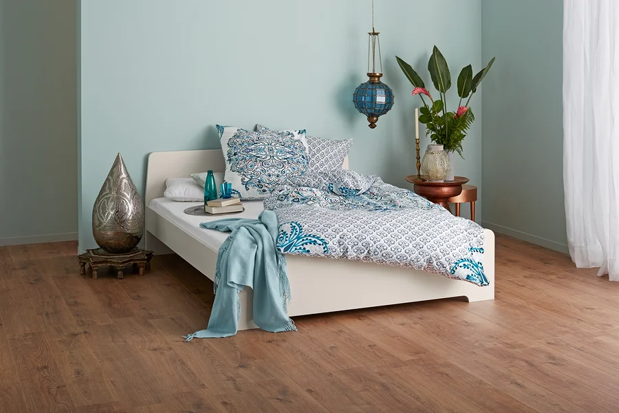 Schlafzimmer mit einem Bett mit blau-weißer Bettwäsche, Lampe und dekorativen Elementen.