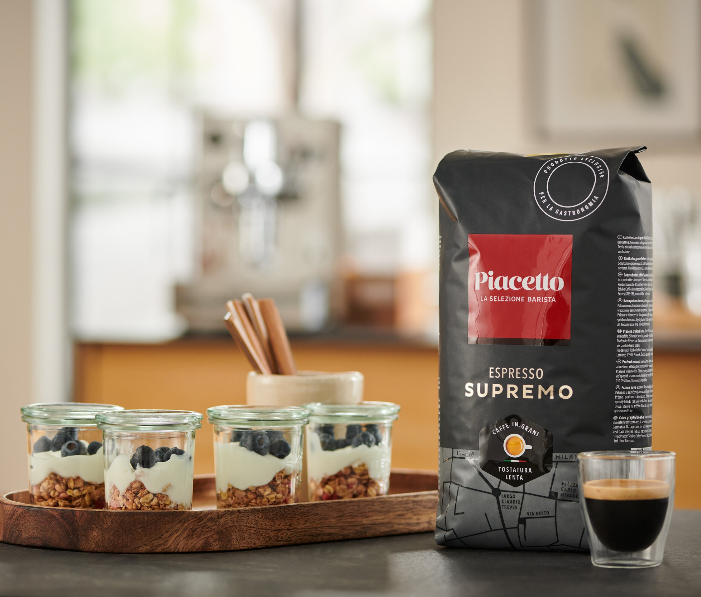 Auf einem Tisch stehen vier Gläser mit Joghurt und Blaubeeren, eine Packung Piacetto Espresso Supremo und eine Tasse Espresso.