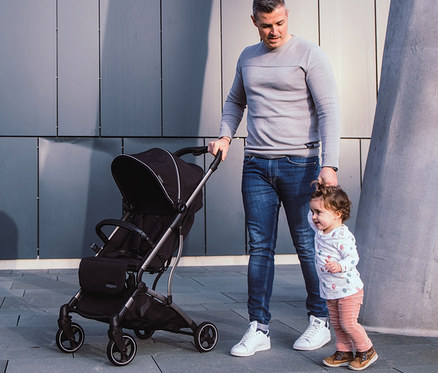 Mann schiebt schwarzen Osann Sportwagen »Boogy« und hält ein kleines Kind an der Hand.