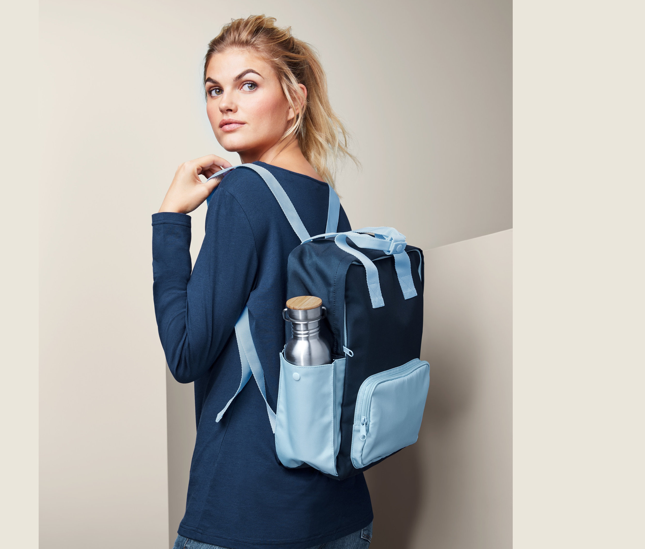 Frau mit Outdoor-Rucksack, Heritage. In der Seitentasche befindet sich eine Trinkflasche.