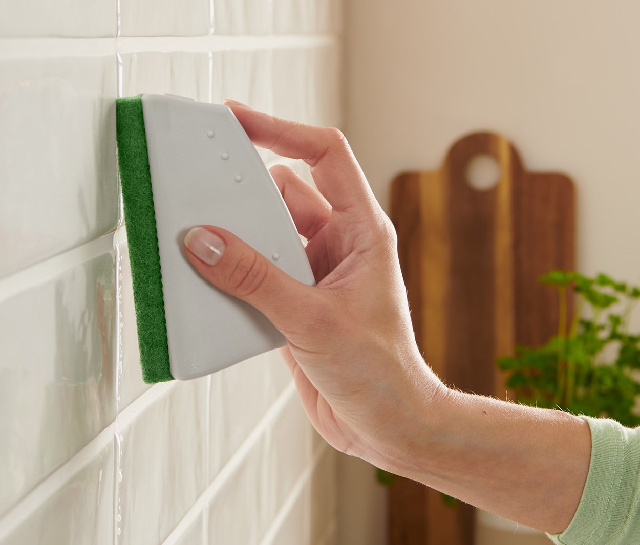 Frau reinigt weiße Fliesen mit Kanten-und-Fugen-Schaber.