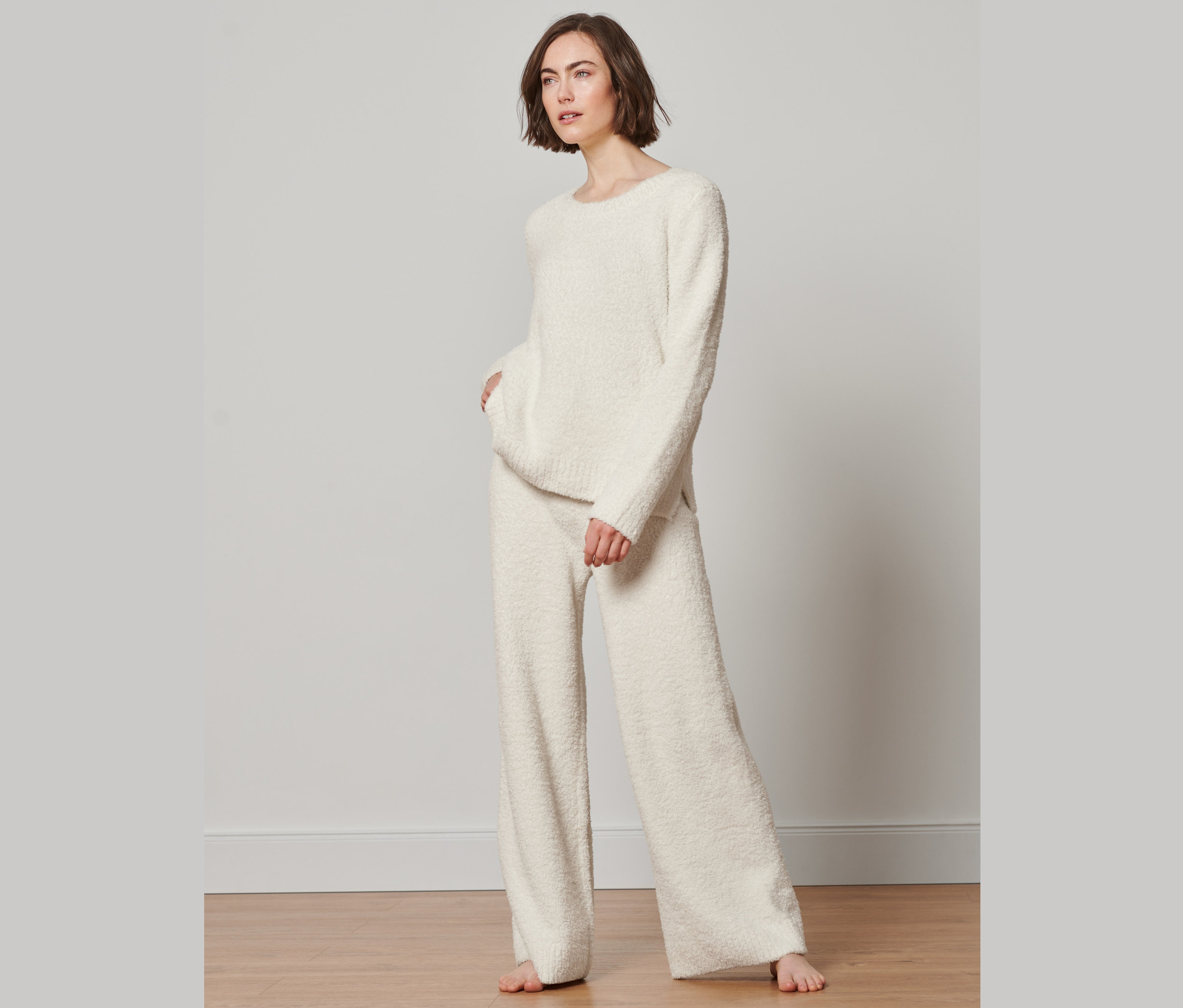 Frau posiert in cremefarbenem Pullover und Loungehose.