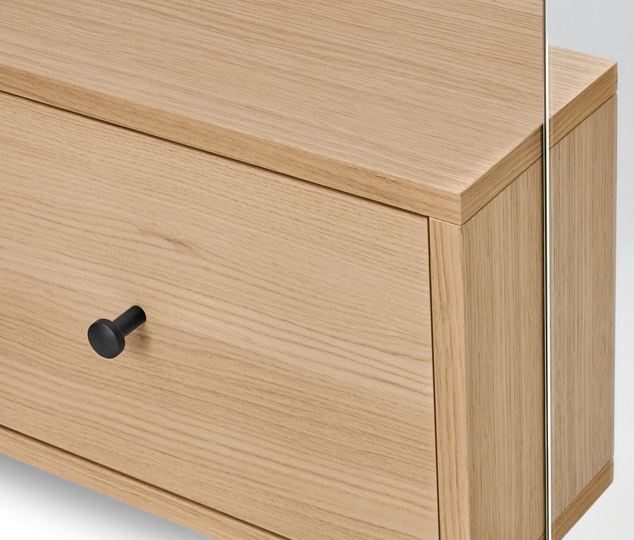 Detailaufnahme einer hellen Holzkommode mit Schublade, einem runden, schwarzen Griff und einem Spiegel.