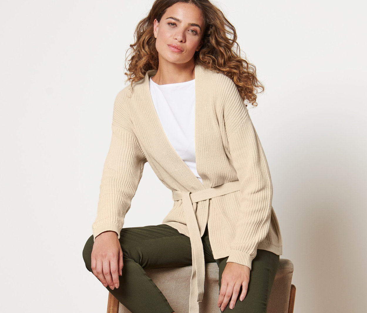 Frau sitzt auf einem Stuhl und trägt einen Wickel-Cardigan.