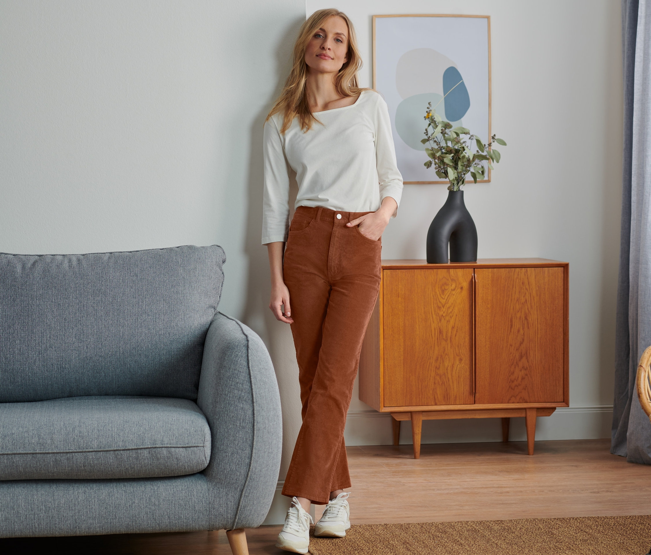 Frau posiert in ausgestellter Cordhose und weißem Oberteil.