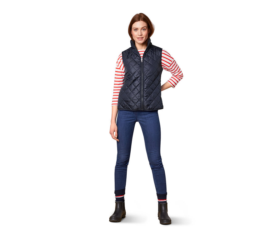 Frau posiert in marineblauer Steppweste und Jeans. Sie trägt eine 3-in-1-Regenjacke.