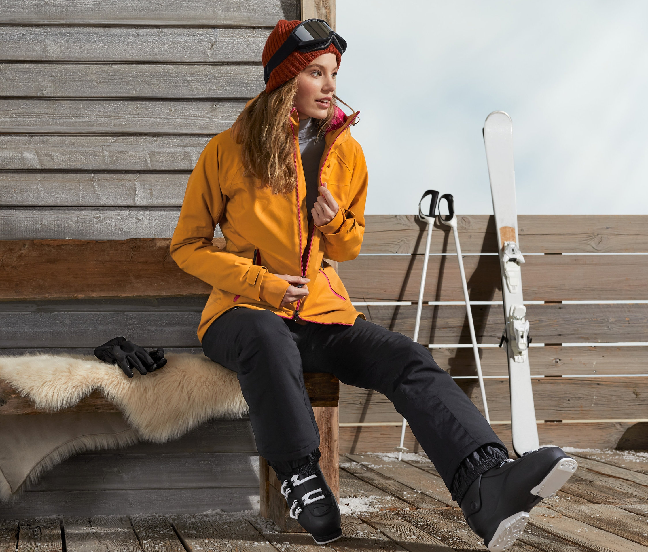 Frau sitzt auf Bank mit Skijacke und Skischuhen.