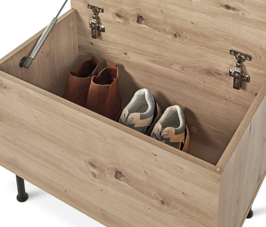 Eine geöffnete Sitzbank mit Stauraumfach, in der sich zwei braune Stiefel und zwei Paar Turnschuhe befinden.