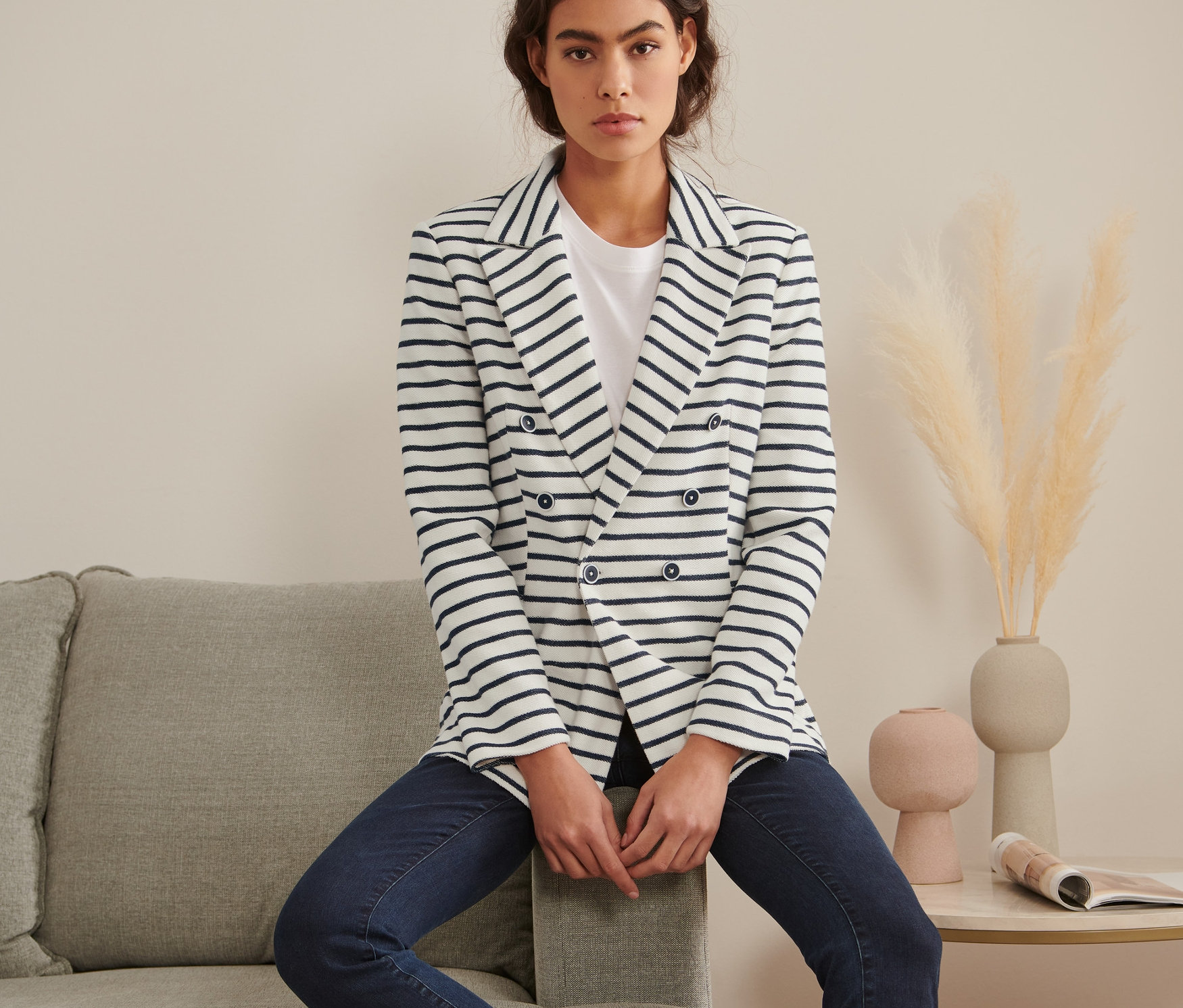 Frau sitzt auf grauem Sofa und trägt einen gestreiften Sweatblazer.