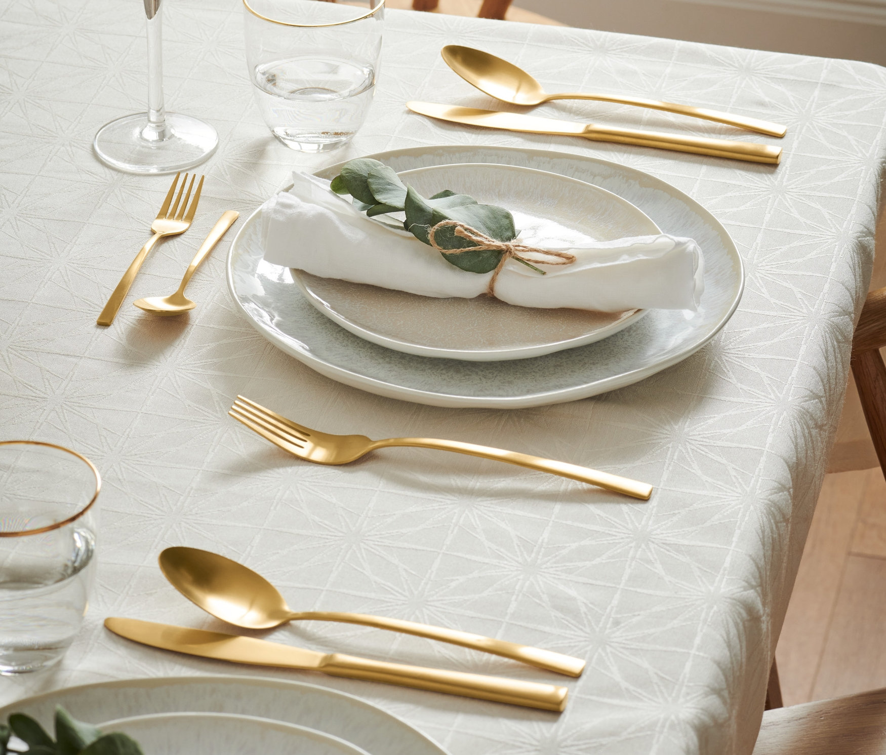 Gedeckter Tisch mit Tellern, Gläsern und goldenem Besteck-Set.