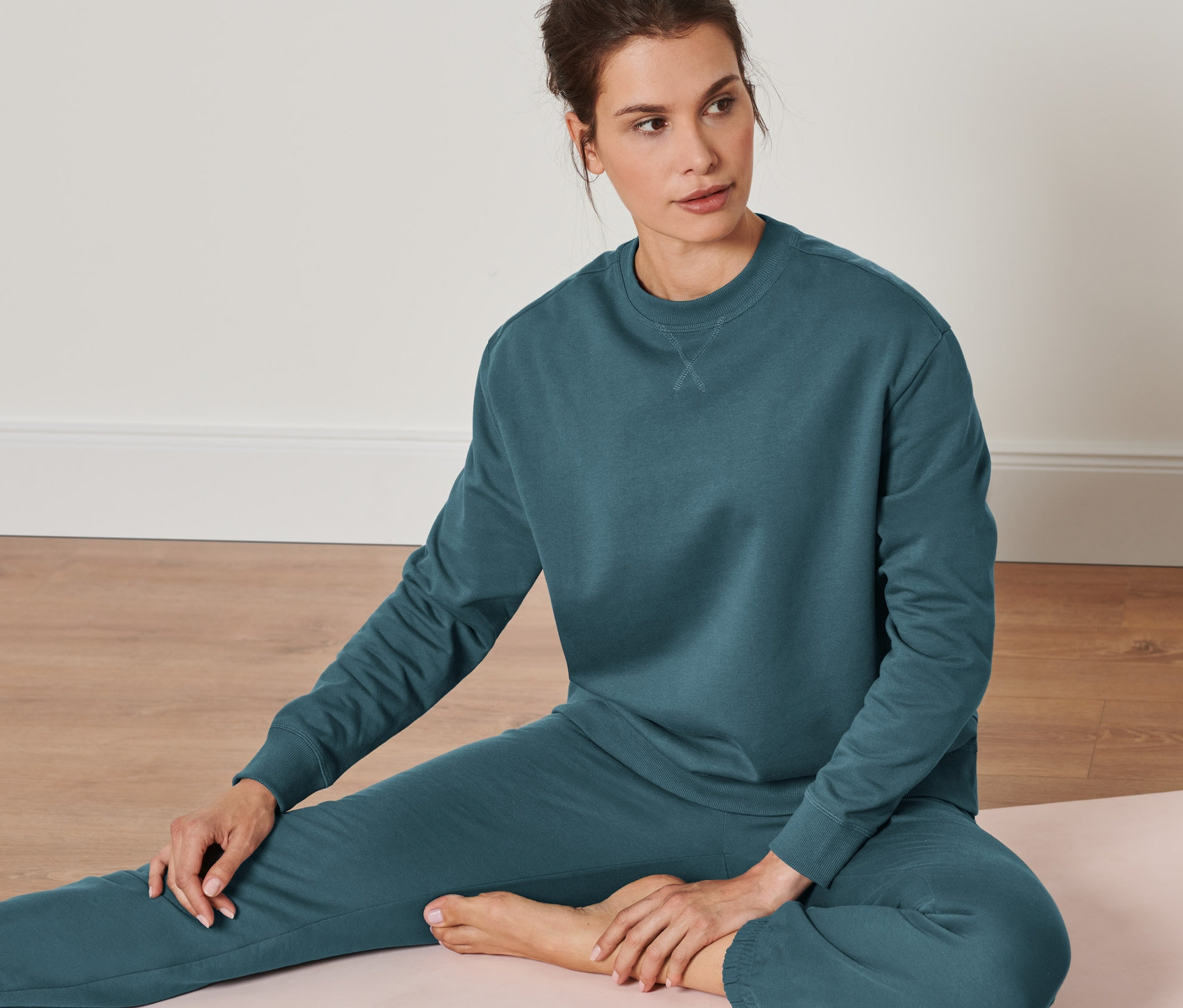 Eine Frau sitzt auf einer Yogamatte und trägt ein Oversized Yogasweatshirt, dunkelsmaragdgrün.