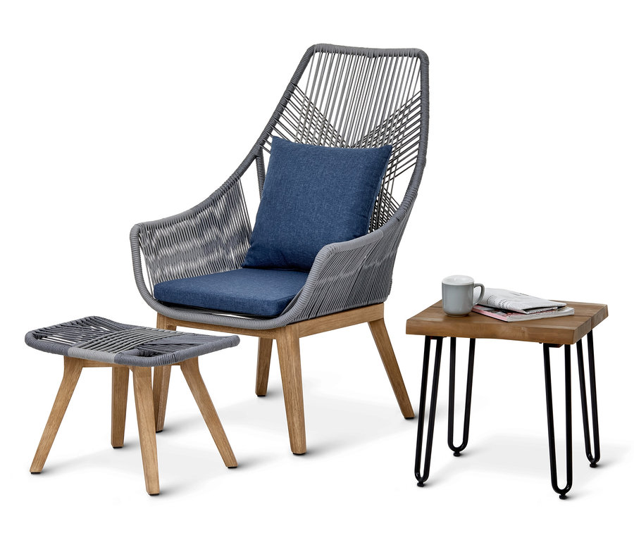 Grauer Sessel mit Hocker und blauen Kissen neben Garten-Beistelltisch.