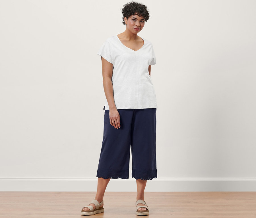 Frau posiert in einem cremeweißen Shirt aus Leinenmix, einer dunkelblauen Culotte mit Stickerei und Plateau-Sandalen aus Leder.