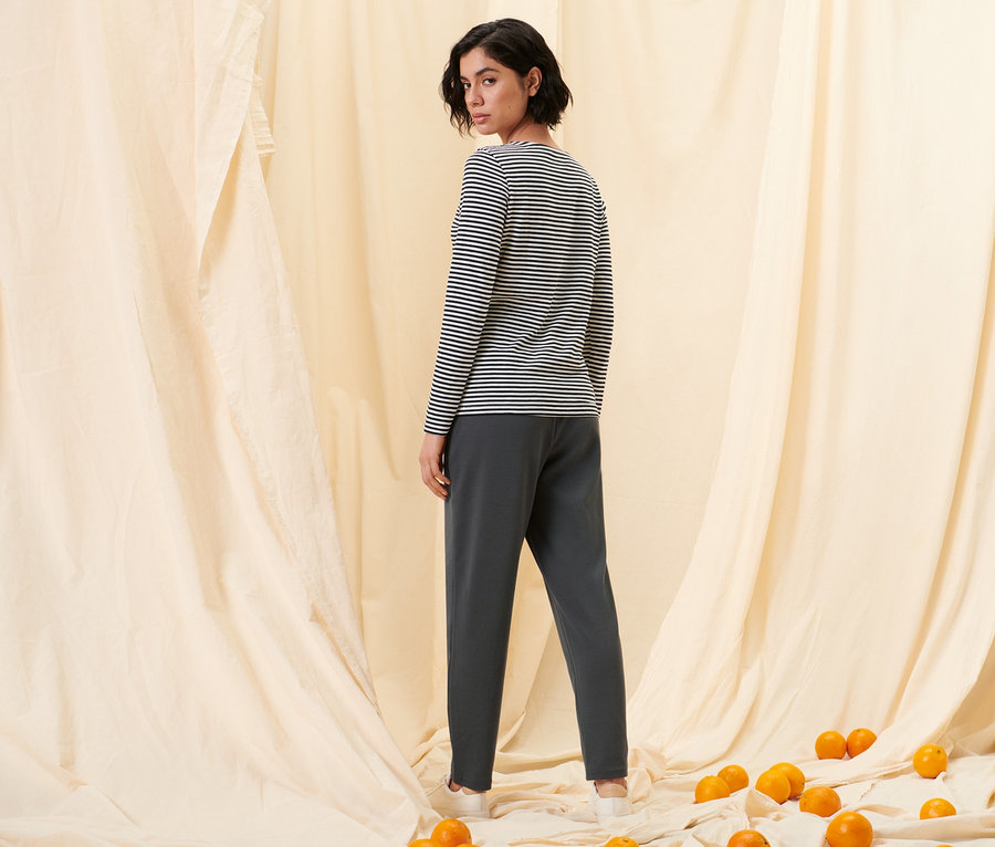 Eine Frau blickt über die Schulter und trägt ein gestreiftes Langarmshirt, schwarz, und eine Joggpants mit Biese.