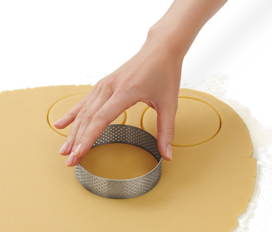 Eine Hand sticht mit einem Edelstahl-Backring Kreise aus Teig aus.