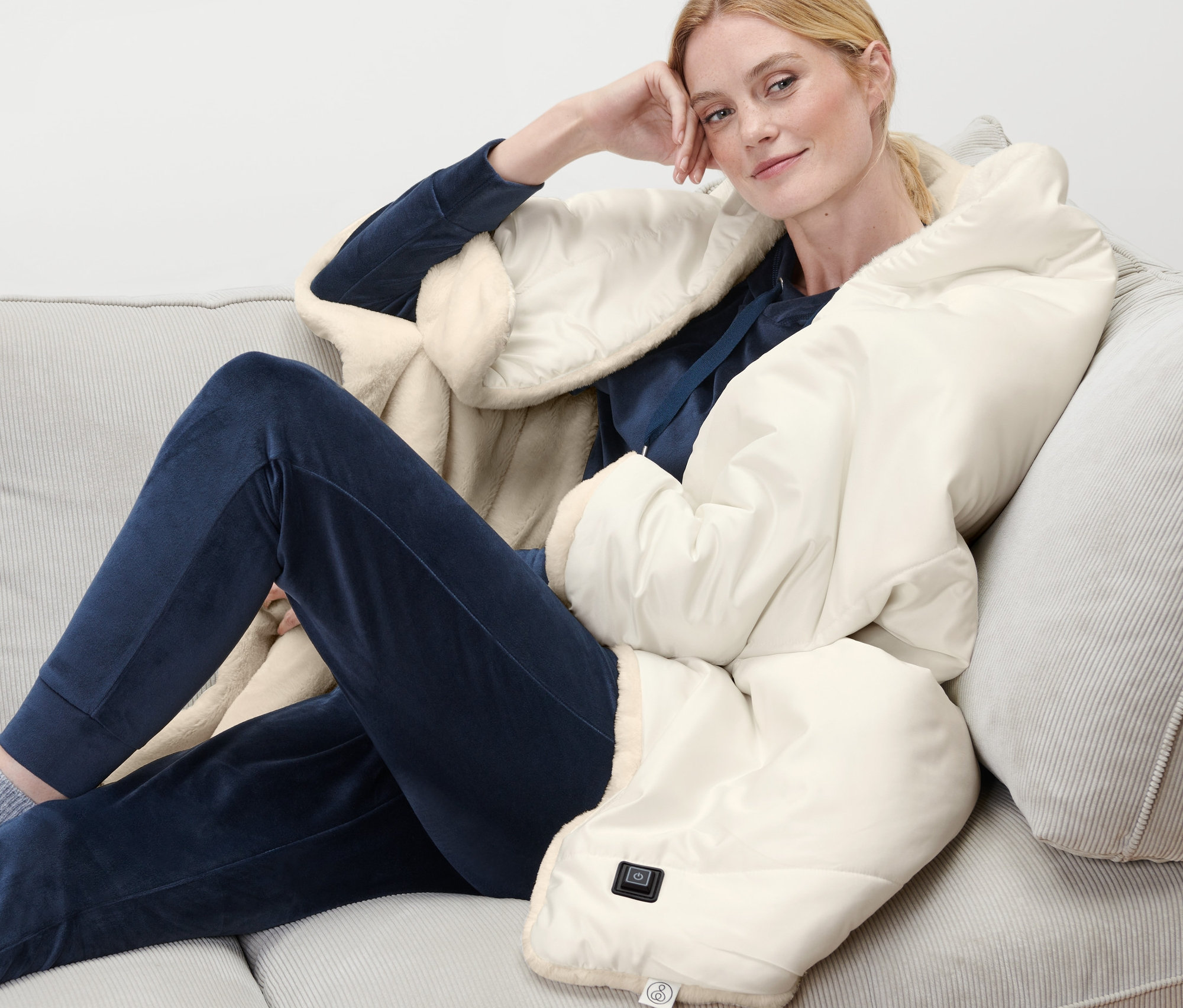 Frau sitzt mit Akku-Heizponcho auf Sofa.