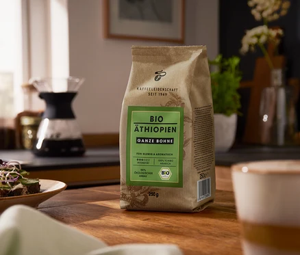 Auf einem Holztisch steht eine Packung Bio Äthiopien - 250 g Ganze Bohne. Im Hintergrund befindet sich eine Kaffeemaschine.