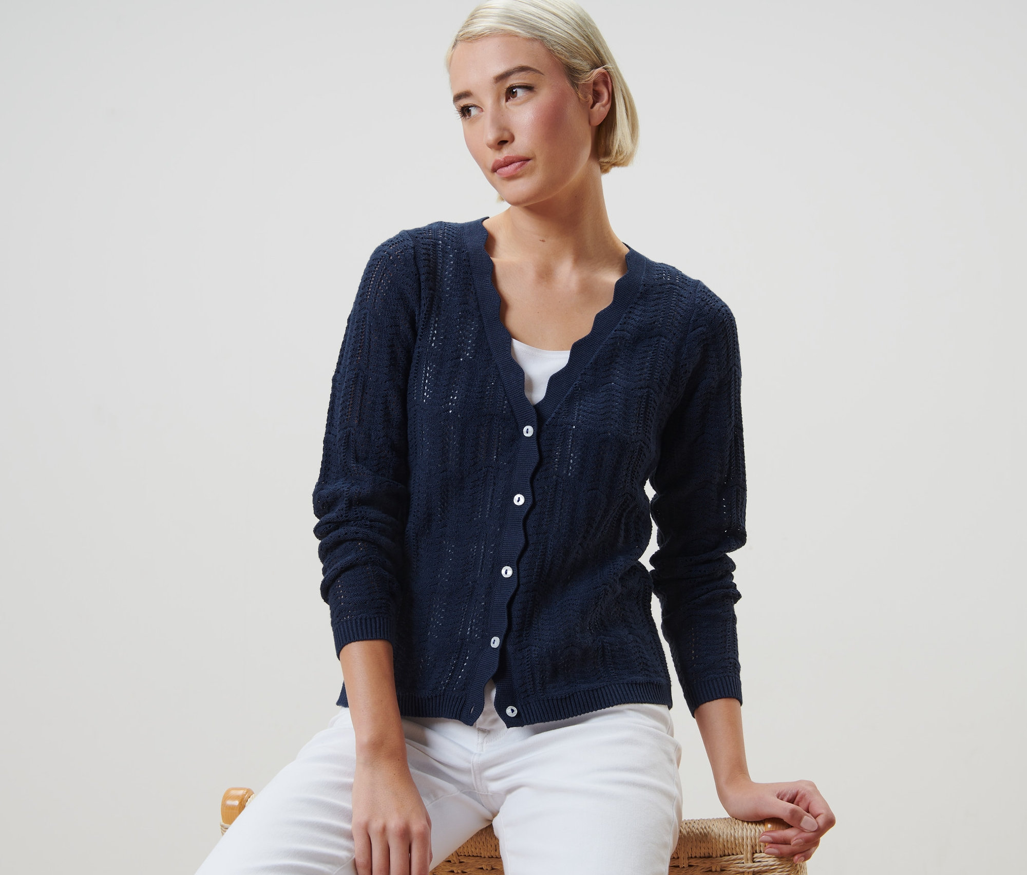 Frau sitzt und trägt eine Strickjacke mit Ajour-Muster.