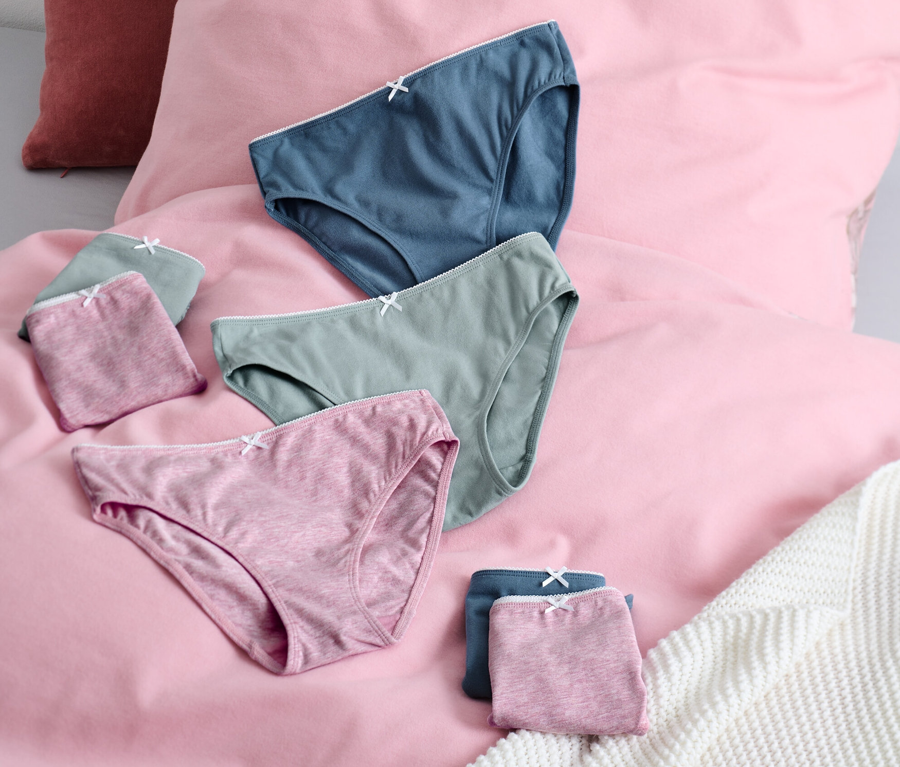 Auf einem rosa Bettlaken liegen 7 Mädchen-Slips in den Farben Blau, Grün und Rosa.