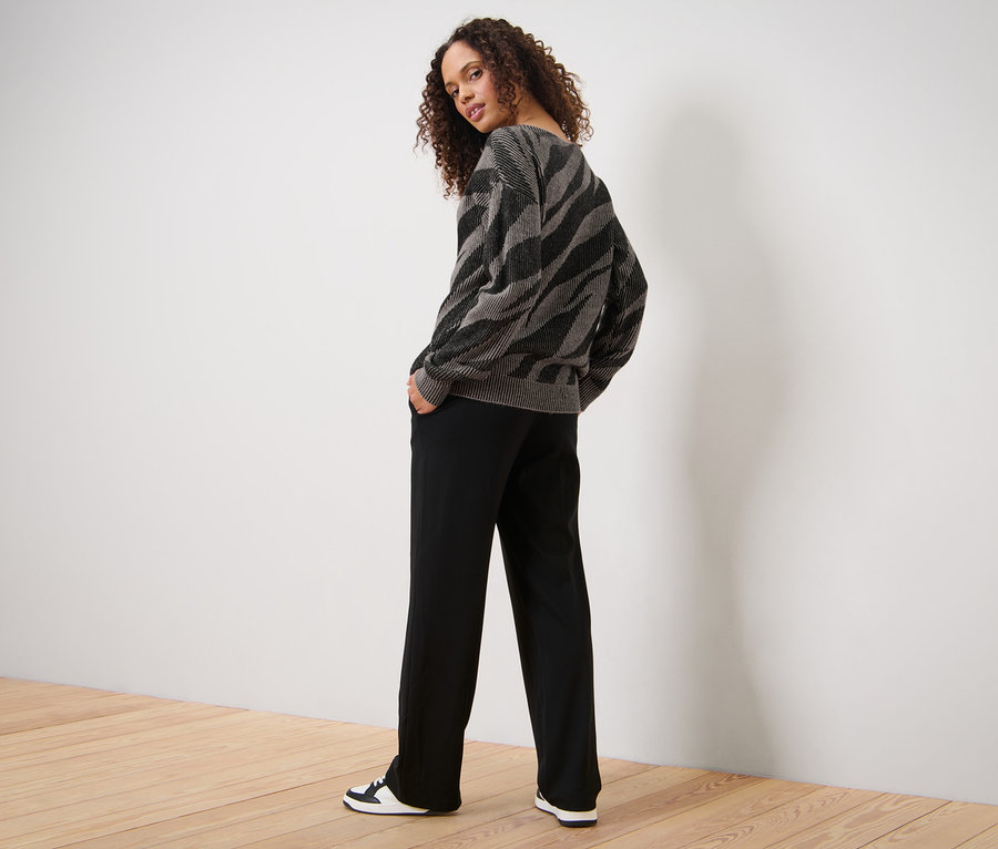 Frau posiert in Strickpullover mit Jacquard, schwarzen Hosen und Turnschuhen.