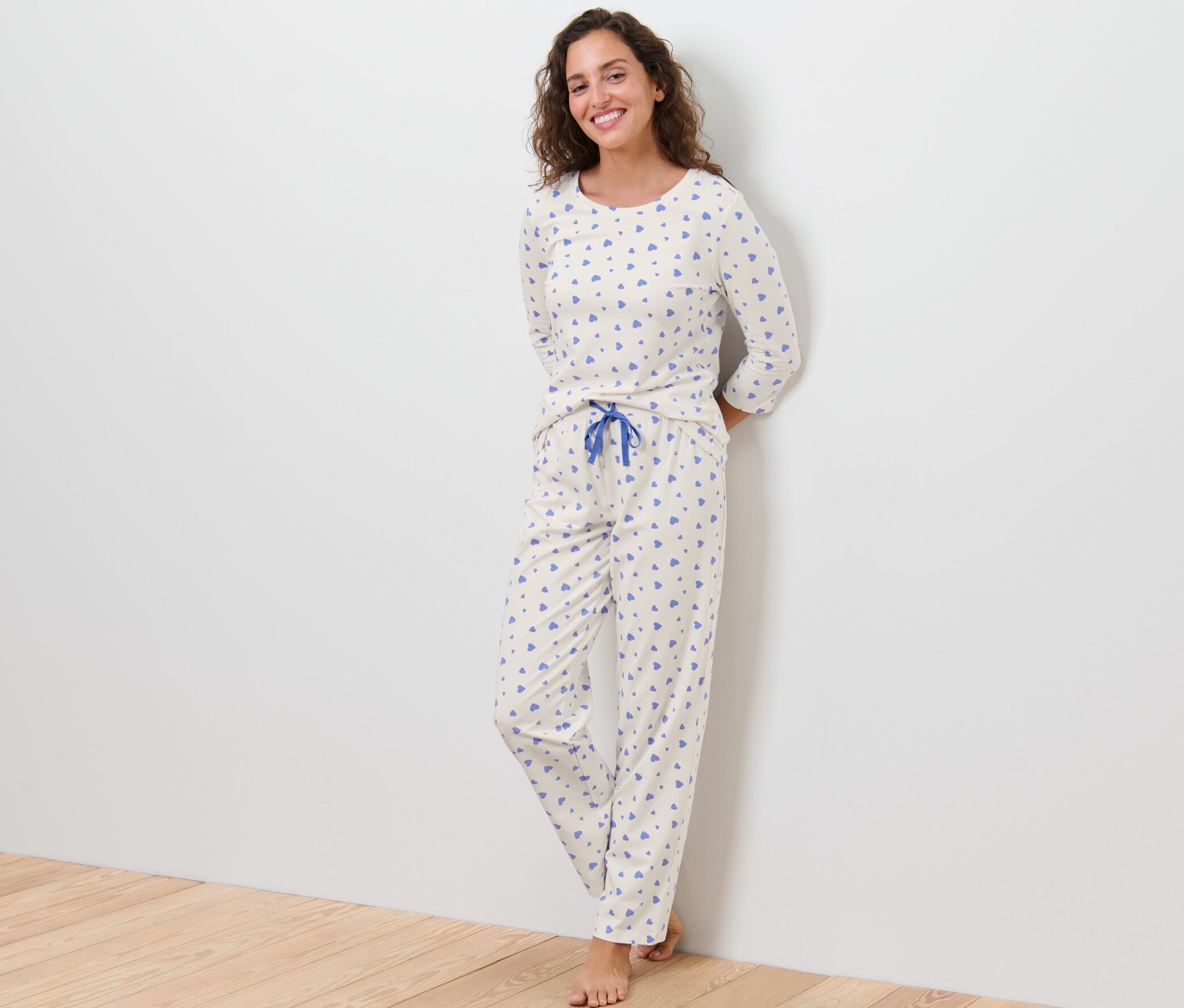 Frau steht an einer Wand und trägt einen Pyjama mit Herzen.